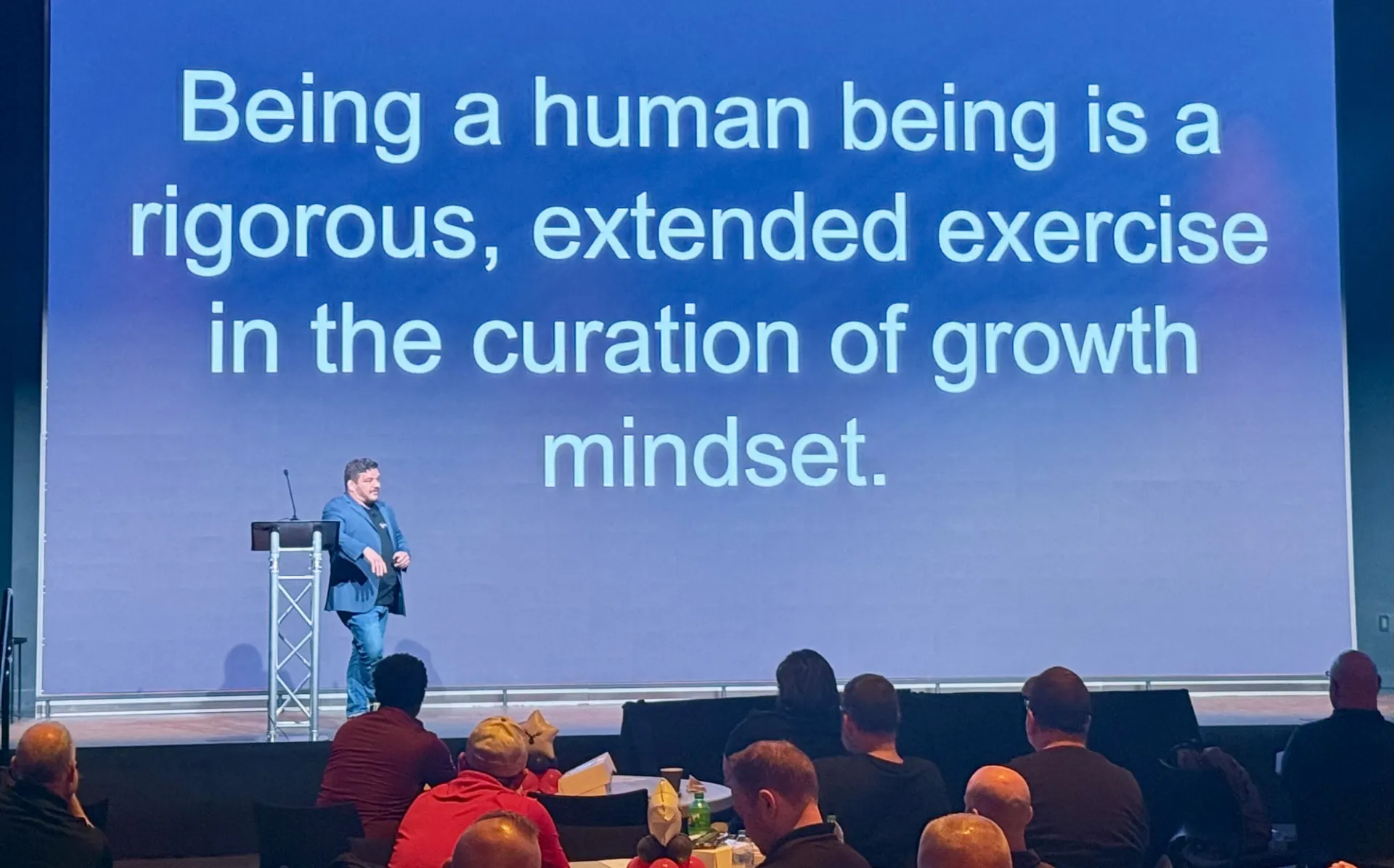 RJ Jenkins presenting at The Amazon Mission Forward Veteran Summit. Slide says" Being a human being is a rigorous, extended exercise in the curation of growth mindset.